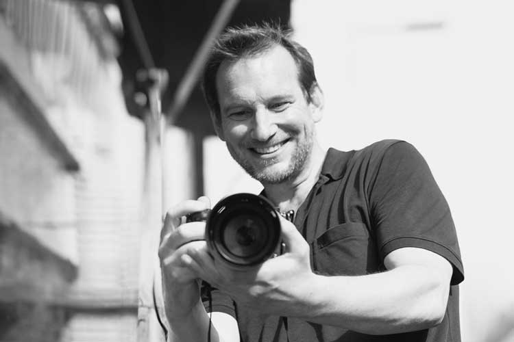 Selbstportrait von Fotograf Kolja Raschke lächelnd mit seiner Kamera in der Hand